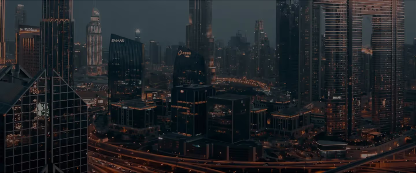 Luchtfoto van een verlichte stedelijke skyline met hoge wolkenkrabbers en drukke snelwegen ’s avonds.